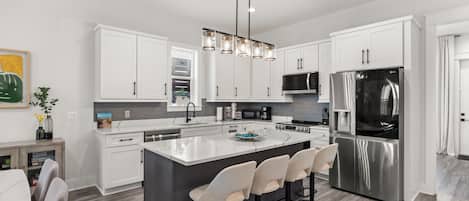 A modern kitchen with white cabinets, a central island with bar stools, stainless steel appliances, and pendant lighting.