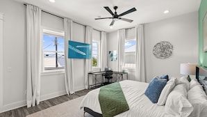 A bedroom with a bed, a desk, a chair, a ceiling fan, and a TV.