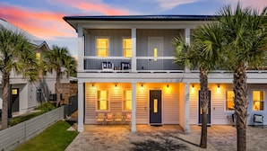 A two-story house with a balcony, a driveway, and palm trees.