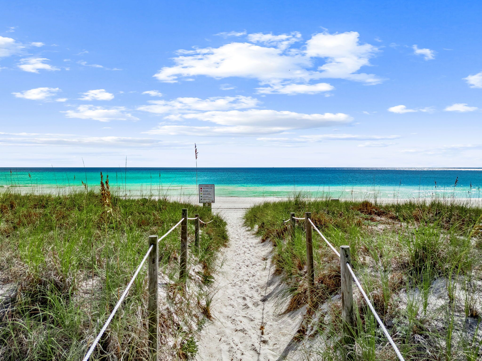 A sandy beach path leading to the ocean with a signpost in the center.