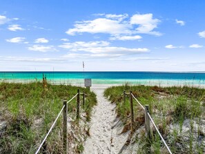 Un sentier de sable qui longe la plage et mène à l’océan, avec un panneau indicateur au milieu.