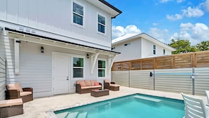 A modern two-story house with a swimming pool, outdoor seating, and a wooden fence.