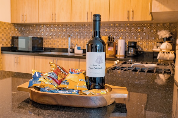 Een fles wijn op een houten dienblad met lekkernijen in een keuken.