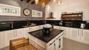 Una cocina moderna con armarios blancos, encimeras negras y lámparas colgantes. Hay un reloj en la pared y una ventana sobre el fregadero.