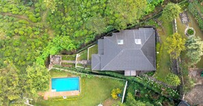 Une vue aérienne d’une maison avec une piscine, entourée d’une végétation luxuriante et d’un chemin en pierre.