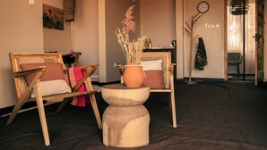A room with two wooden chairs, a small round table, a potted plant, and a clock on the wall. - Shibam Campsite (Naberera)