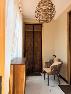 Un pasillo con puerta de madera, una silla de mimbre, una mesa de madera y una lámpara colgante.