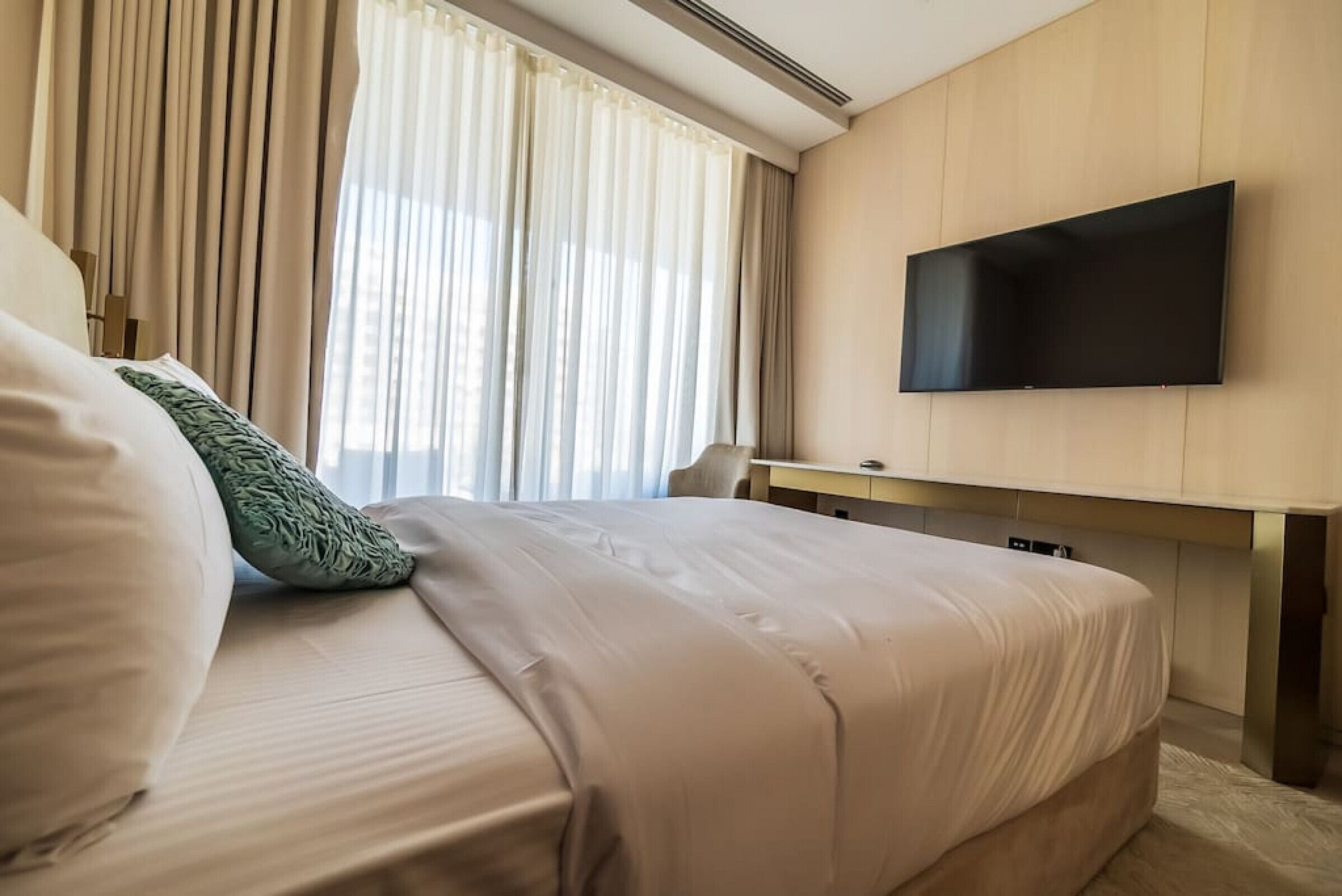 A hotel room with a bed, a desk, and a flat-screen TV mounted on the wall.