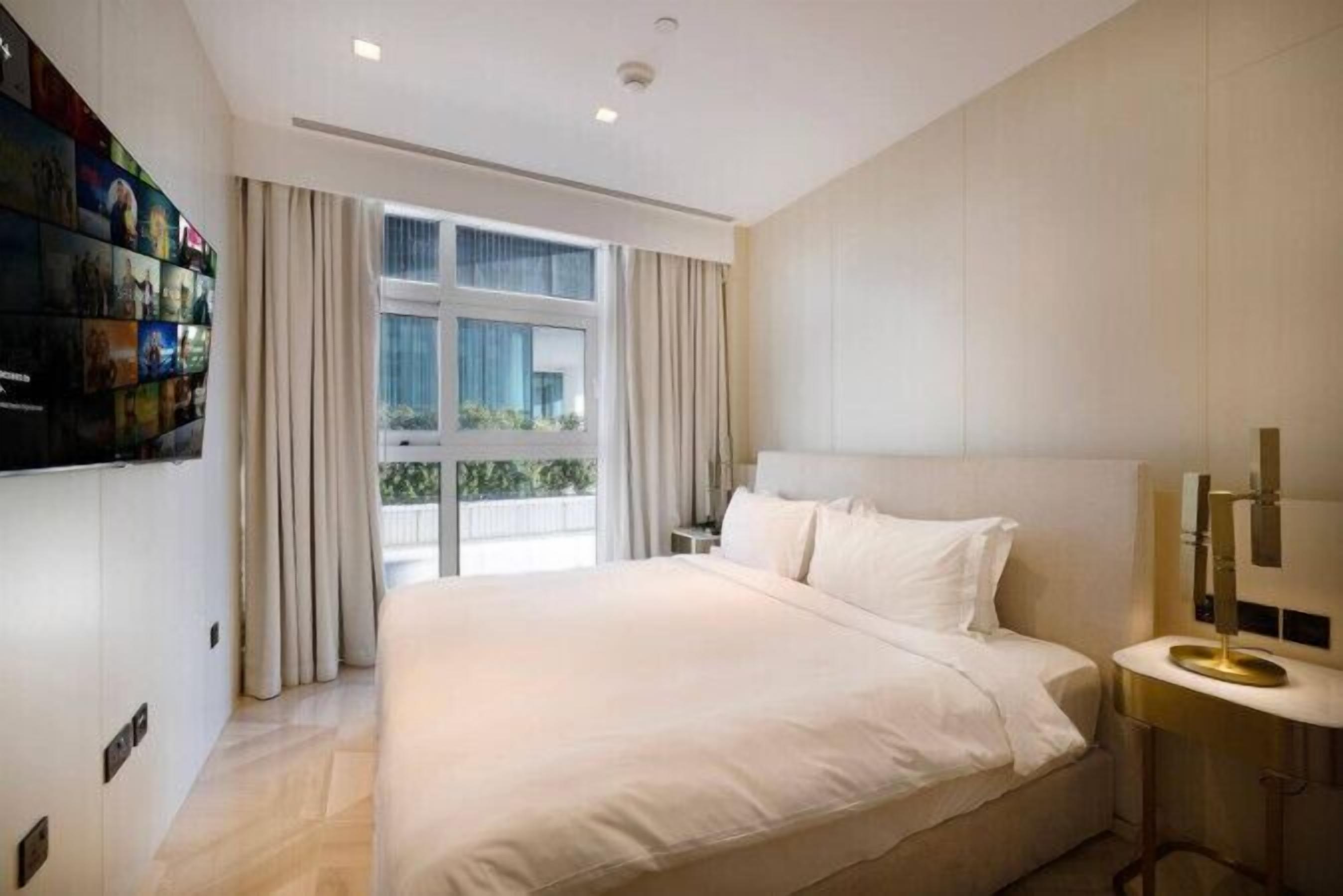 Une chambre d’hôtel moderne avec un grand lit, une table de chevet, un téléviseur fixé au mur et une fenêtre avec des rideaux.