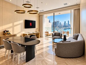 A modern hotel room with a dining area, a flat-screen TV, and a view of a city skyline.