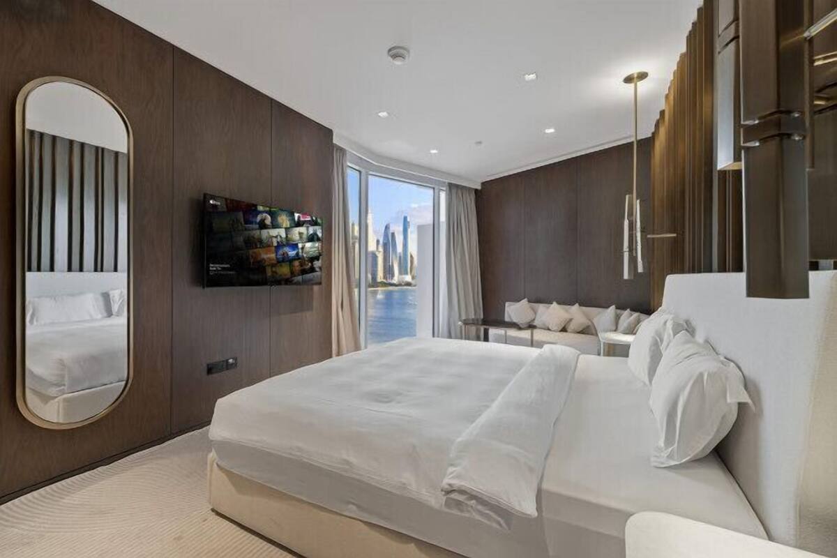 A modern hotel room with a large bed, a TV mounted on the wall, and a view of the cityscape through the window.