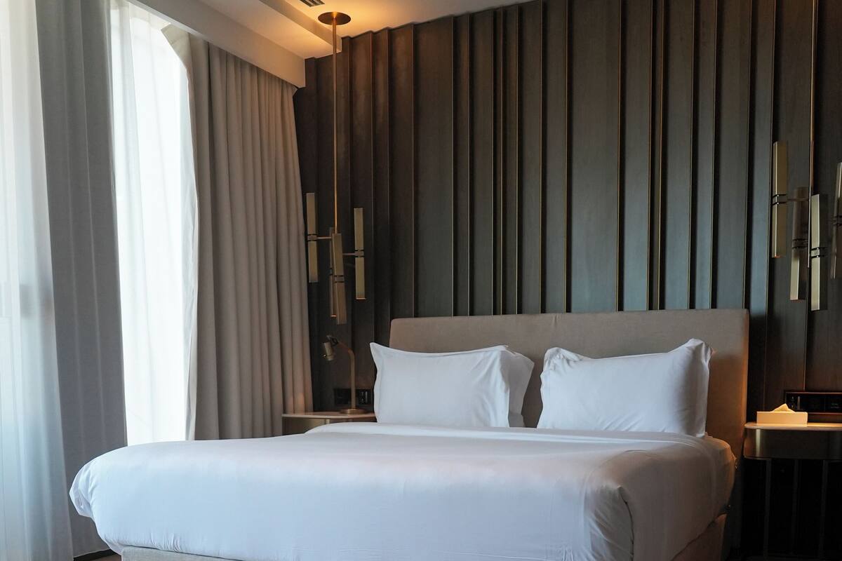 A modern hotel room with a large bed, a nightstand, and a wall-mounted lamp.