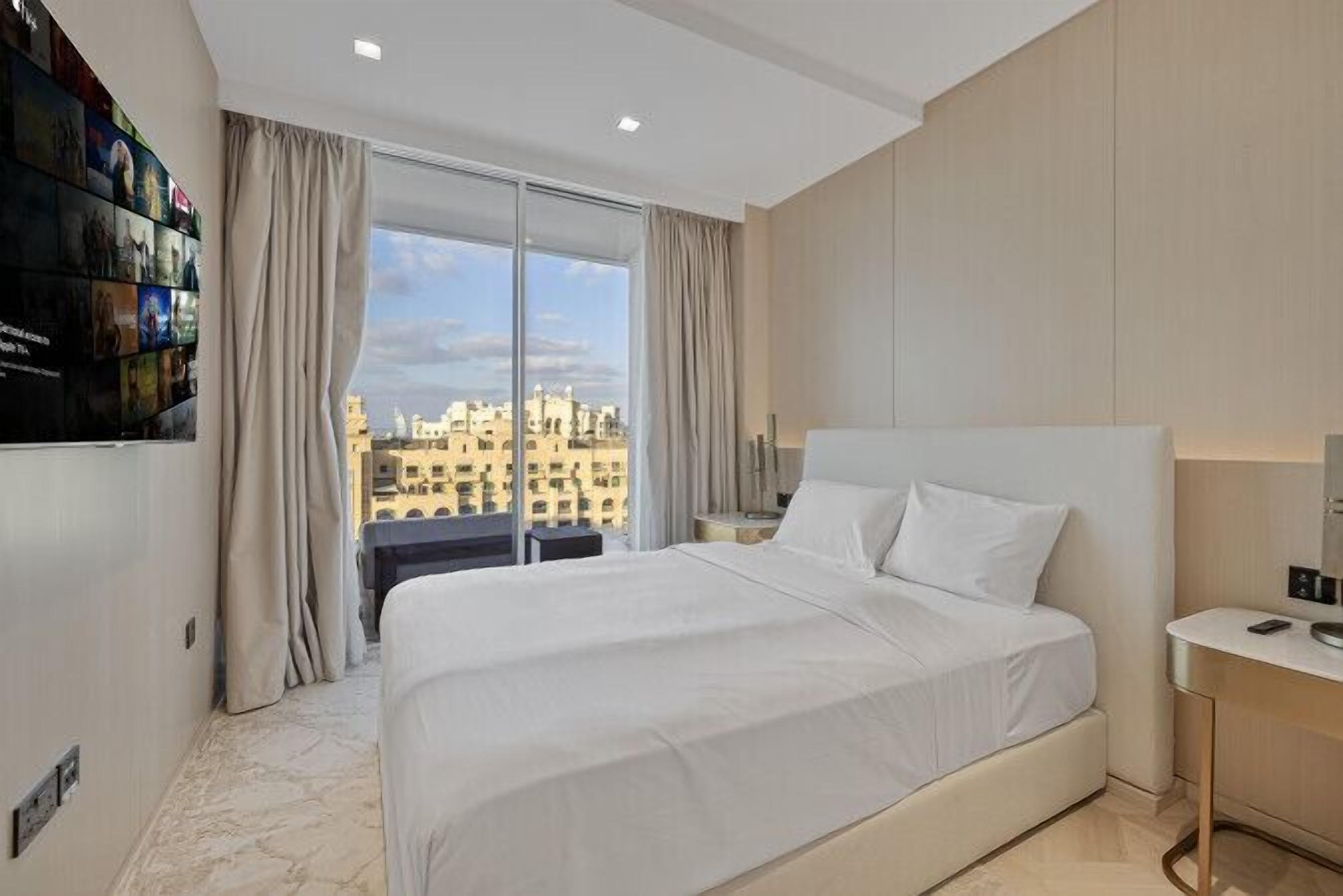 Una habitación de hotel moderna con una cama grande, vistas a la ciudad y un televisor de pared.