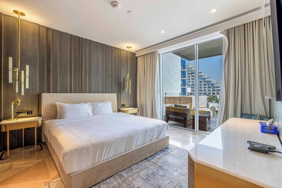 A modern hotel room with a large bed, a desk, and a balcony with a city view.