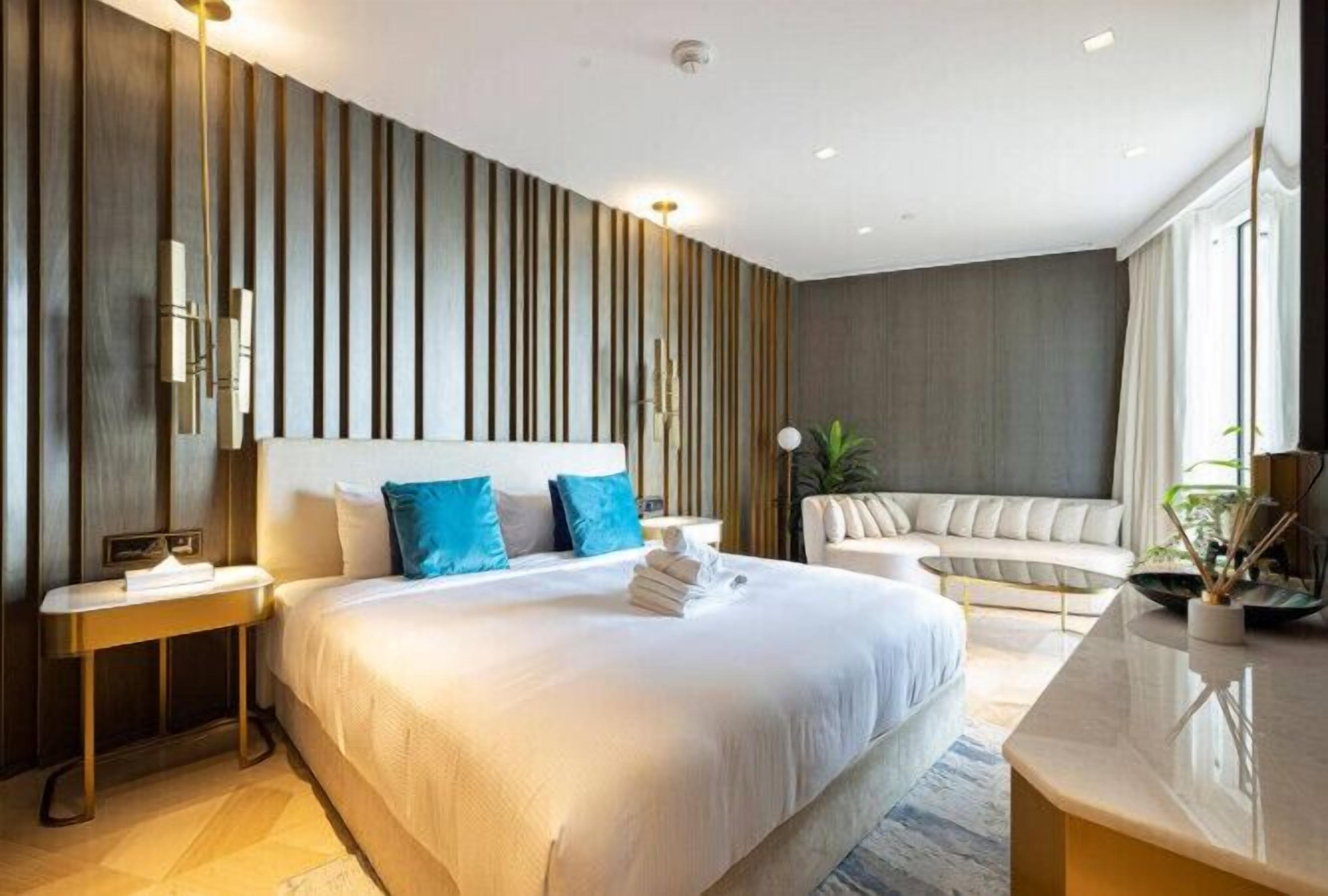 A modern hotel room with a large bed, a sofa, a small table, and a bedside table.