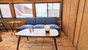 A cozy room with a blue sofa, a small table with a lamp, and a view of a snowy landscape through large windows. - Modern Multi-level Frisco Townhome—Spacious + Central! (Frisco)