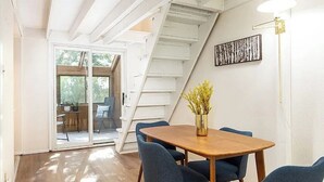 A dining area with a wooden table and blue chairs, a vase with yellow flowers, and a staircase leading to a balcony. - Modern Multi-level Frisco Townhome—Spacious + Central! (Frisco)