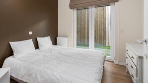 Une chambre avec un grand lit, une commode et une porte-fenêtre coulissante donnant sur un balcon.