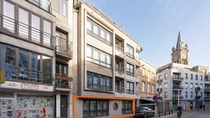 Un immeuble à plusieurs étages, avec un restaurant au rez-de-chaussée, un espace de stationnement pour vélos et, en arrière-plan, le clocher d’une église.