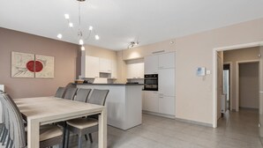 Une cuisine moderne avec des meubles blancs, un îlot central et un coin repas comprenant une table et des chaises.