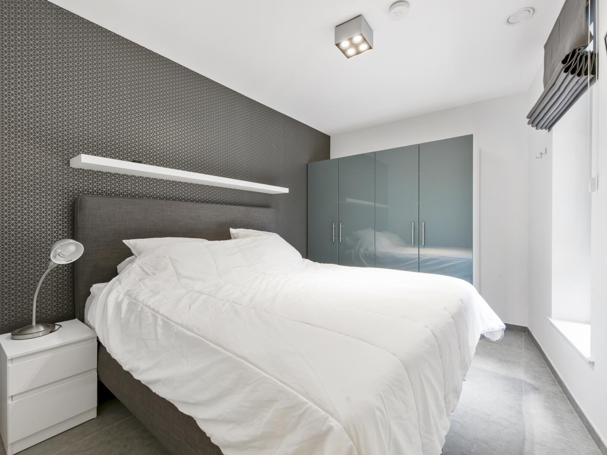 A modern bedroom with a bed, nightstand, and wardrobe.