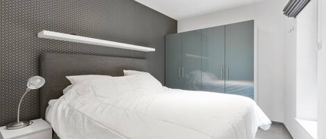 A modern bedroom with a bed, nightstand, and wardrobe.