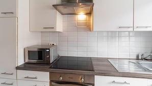A modern kitchen with white cabinets, a built-in microwave, a stove, and a sink. - Ideal holiday home with garage (Blankenberge)