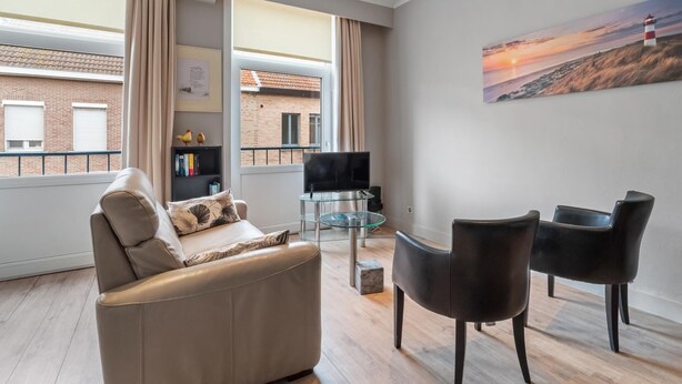 A modern living room with a sofa, two chairs, a TV, and a painting of a sunset. - Ideal holiday home with garage (Blankenberge)