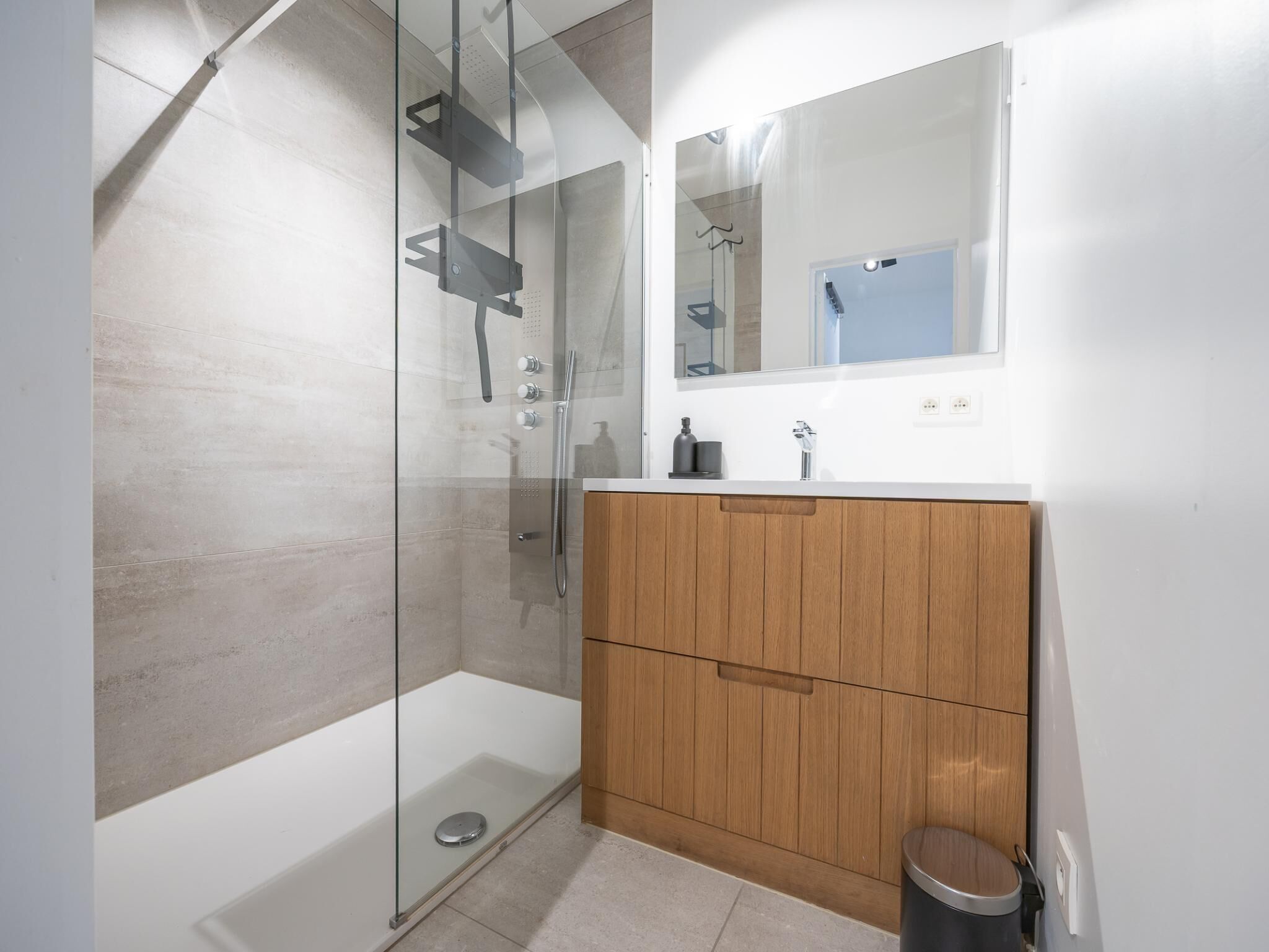 Un baño moderno con ducha de vidrio, tocador de madera y espejo sobre el lavabo.