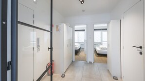 A modern hotel hallway with glass doors, a fire extinguisher, and a visible bed in the adjacent room. - Modern apartment near the sea (Middelkerke)