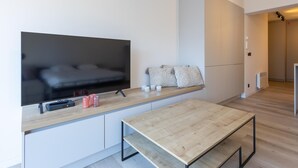 Un espacio habitable moderno y minimalista con un televisor de pantalla plana montado en una pared blanca, una mesa de comedor de madera y un banco.