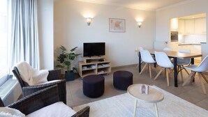 Un salon moderne doté d’un téléviseur à écran plat, d’un coin repas avec une table et des chaises, et d’une cuisine en arrière-plan.