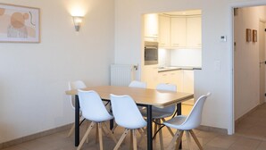 Un coin repas avec une table et des chaises, une cuisine à l’arrière-plan et un tableau encadré au mur.