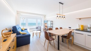 Un espace de vie moderne comprenant un coin repas, une cuisine et une grande fenêtre donnant sur la mer.