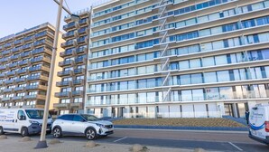 Een modern, meerlaags woongebouw met balkons, een parkeerplaats en een lantaarnpaal.