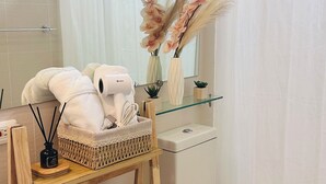 Un baño moderno con un inodoro blanco, un estante de vidrio con objetos decorativos, un estante de madera con una cesta y plantas, y una cortina de ducha.