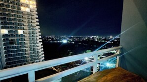 Un balcón con mesa y sillas de madera, con vista a un paisaje urbano nocturno.
