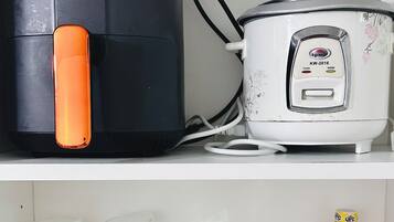 A kitchen with a black appliance and a white rice cooker on the countertop. Below, there are various kitchen items including a jar labeled "Kelly," a wine glass, and several condiment bottles.
