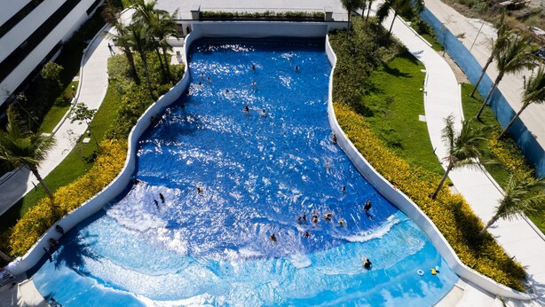 Vista aérea de una amplia piscina curva rodeada de follaje y palmeras.