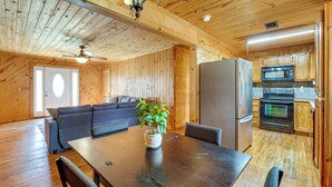 Ein Holzinterieur mit Esstisch, Stühlen, einer Couch, einem Kühlschrank und einer Mikrowelle in einer Küchenzeile.