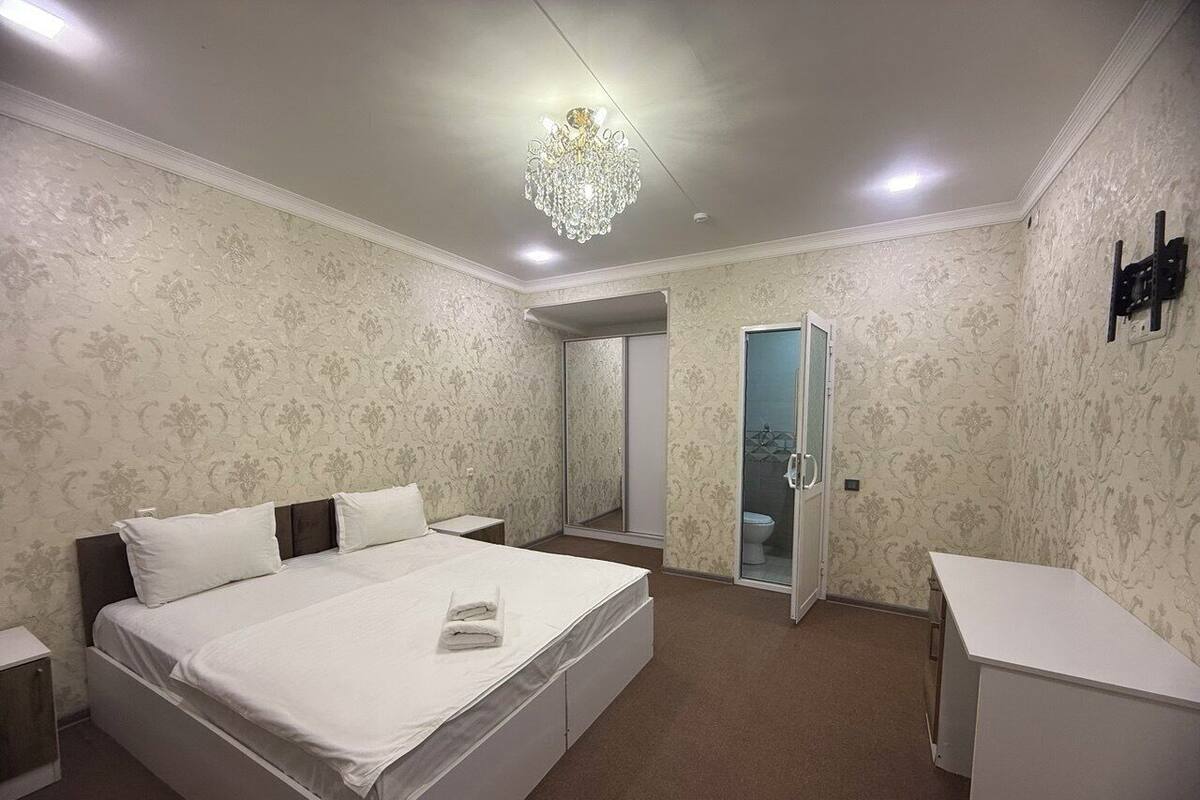 A bedroom with a large bed, a bedside table, a desk, a mirror, and a door leading to a bathroom.