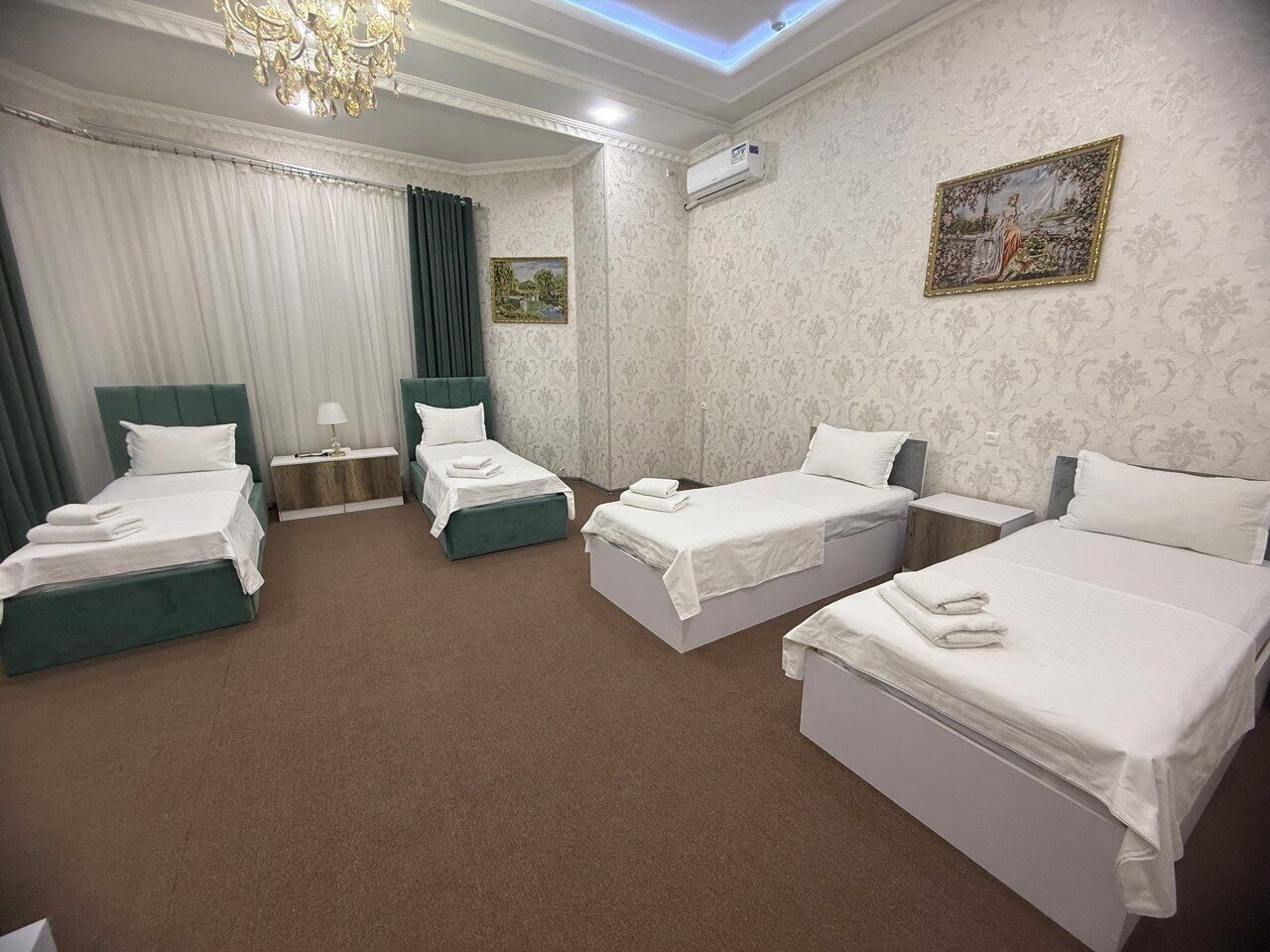 Une chambre d’hôtel avec quatre lits, un lustre, un tableau et une fenêtre avec des rideaux.