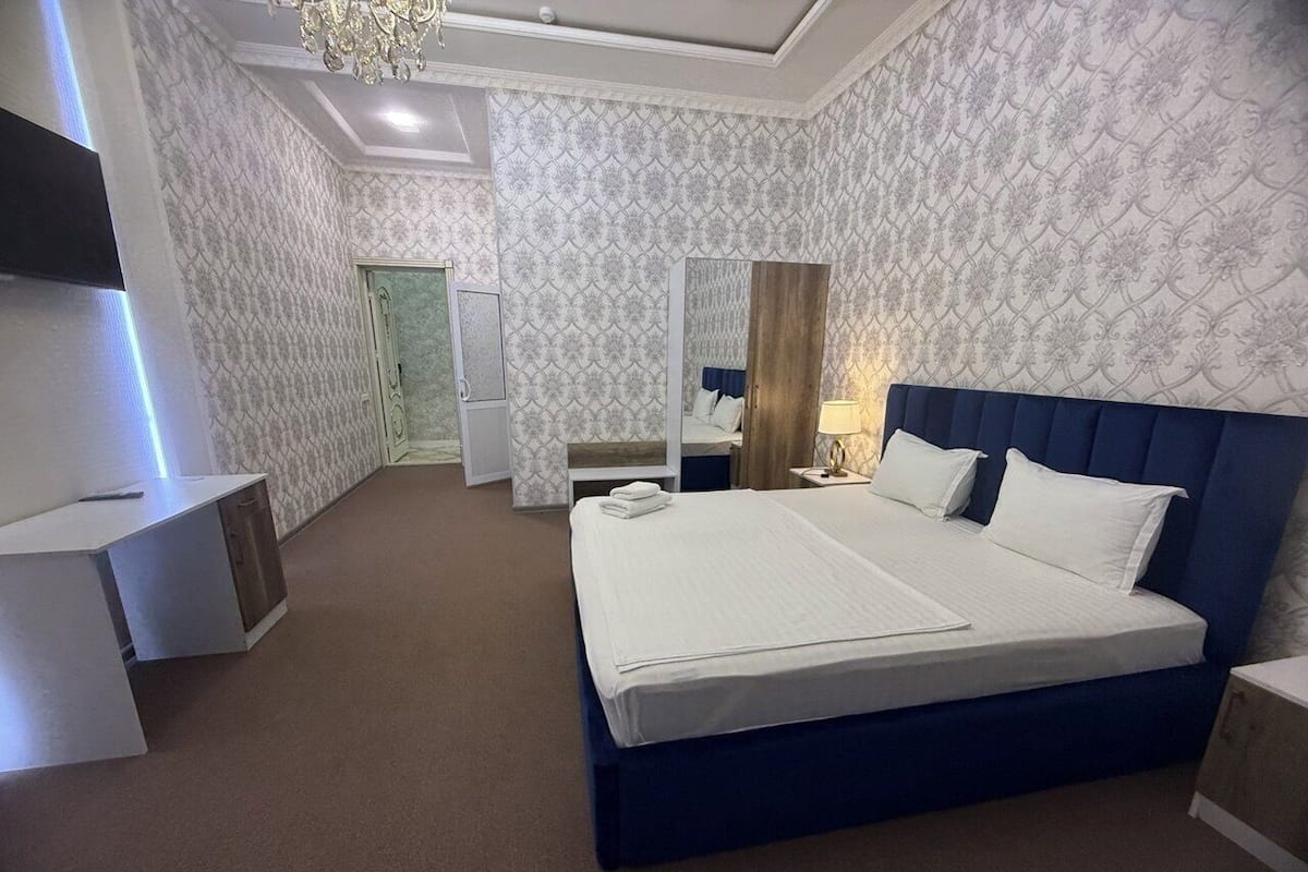 A modern hotel room with a large bed, bedside tables, a desk, and a mirror.