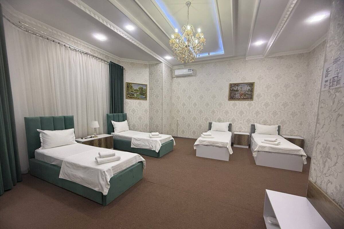 A hotel room with four beds, a chandelier, and a large window with curtains.
