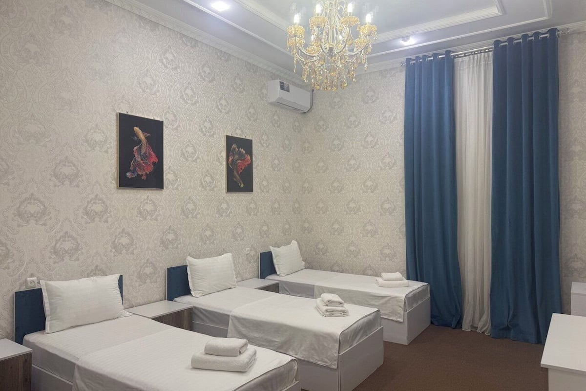 A hotel room with four beds, a chandelier, and two framed pictures on the wall.