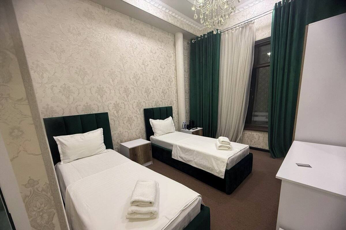 A hotel room with two beds, a desk, a chair, a wardrobe, and a window with curtains.