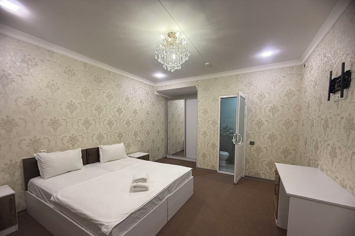 Une chambre à coucher avec un grand lit, une table de chevet, un bureau, un miroir et une porte donnant sur une salle de bain.