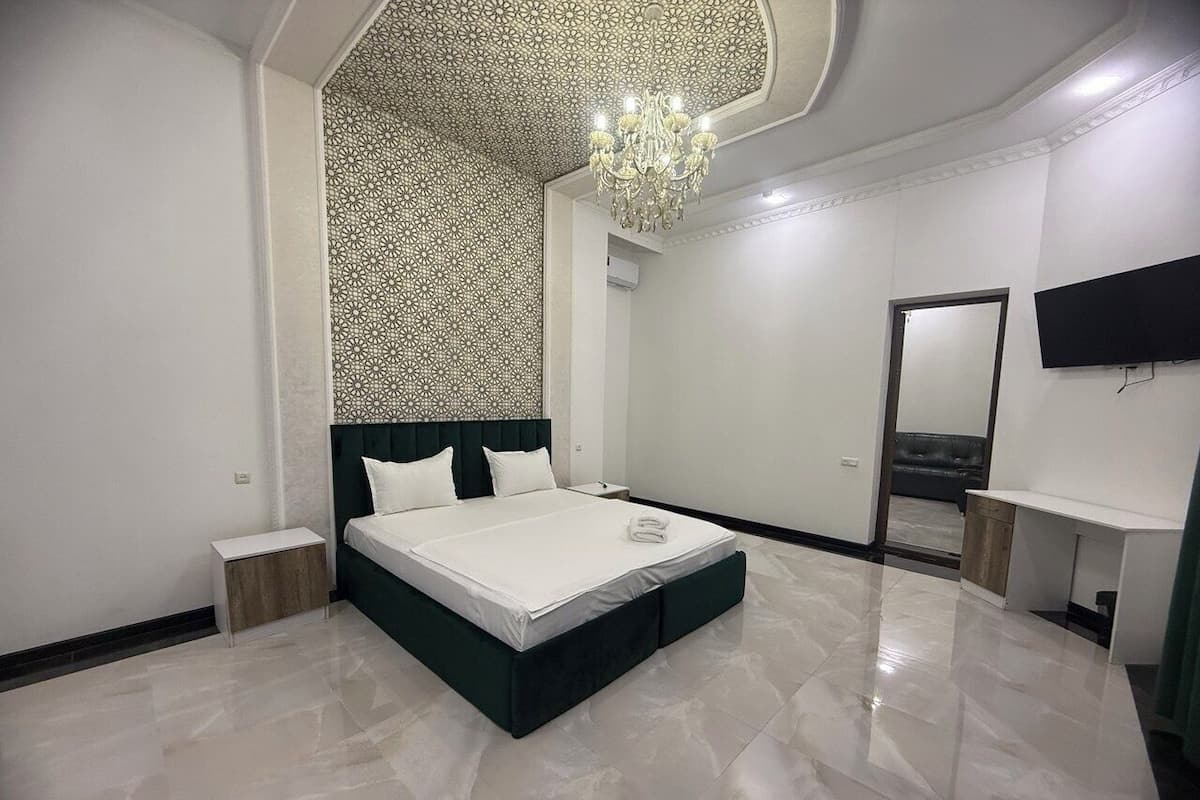 A modern bedroom with a large bed, a chandelier, a flat-screen TV, and a mirror on the wall.