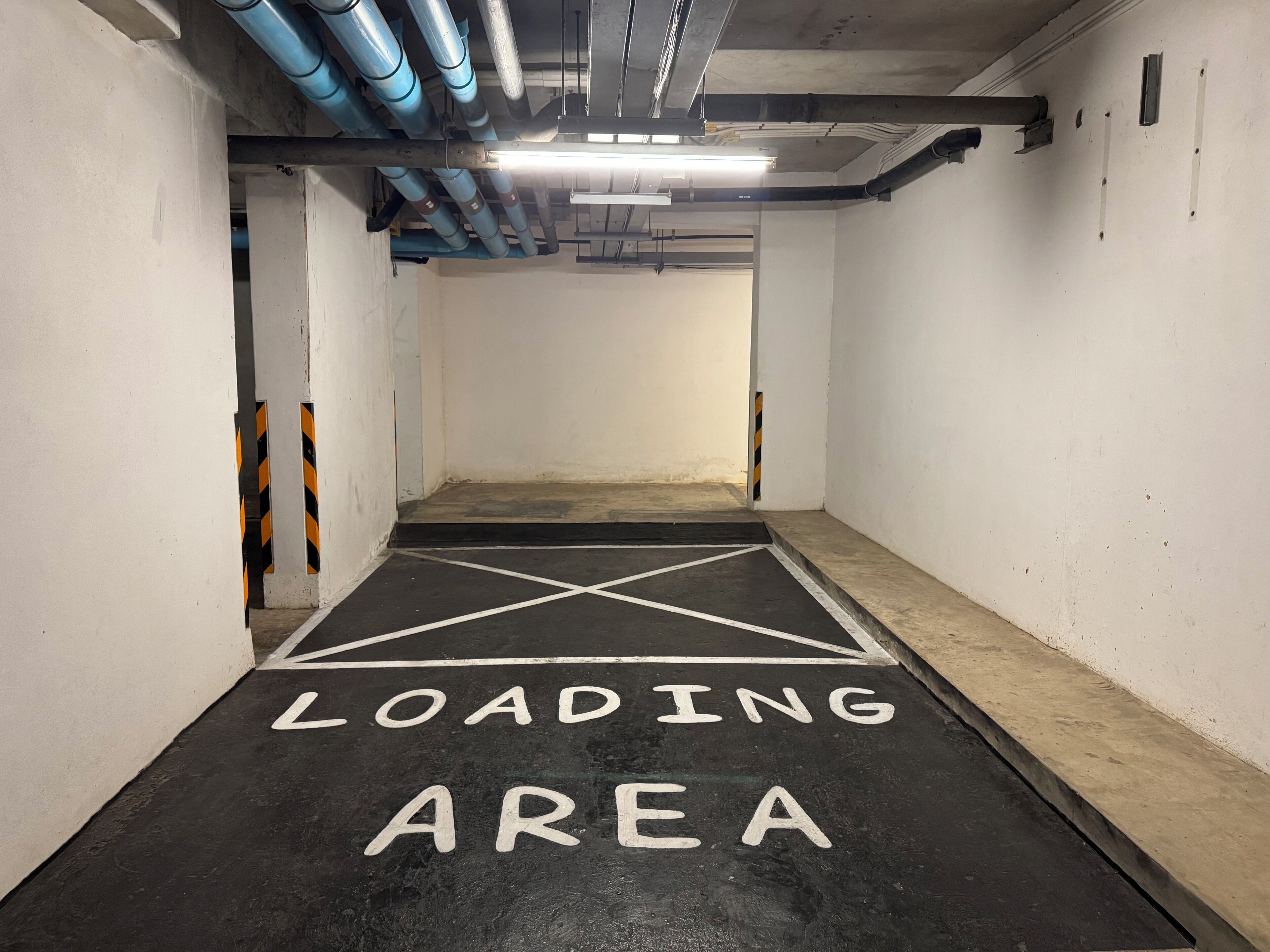 Een laadzone in een parkeergarage met witte wanden en een zwarte vloer, gemarkeerd met de tekst 'LOADING AREA'.