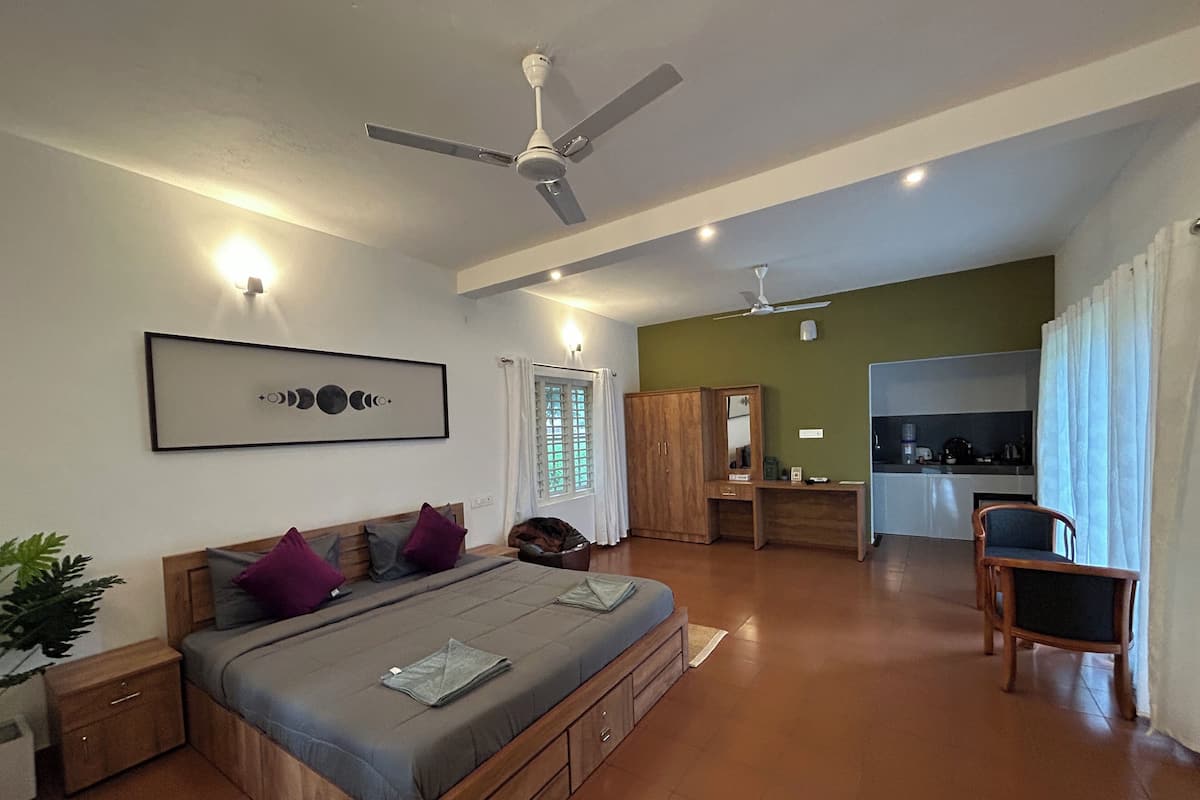 A bedroom with a bed, a desk, a wardrobe, and a kitchenette.